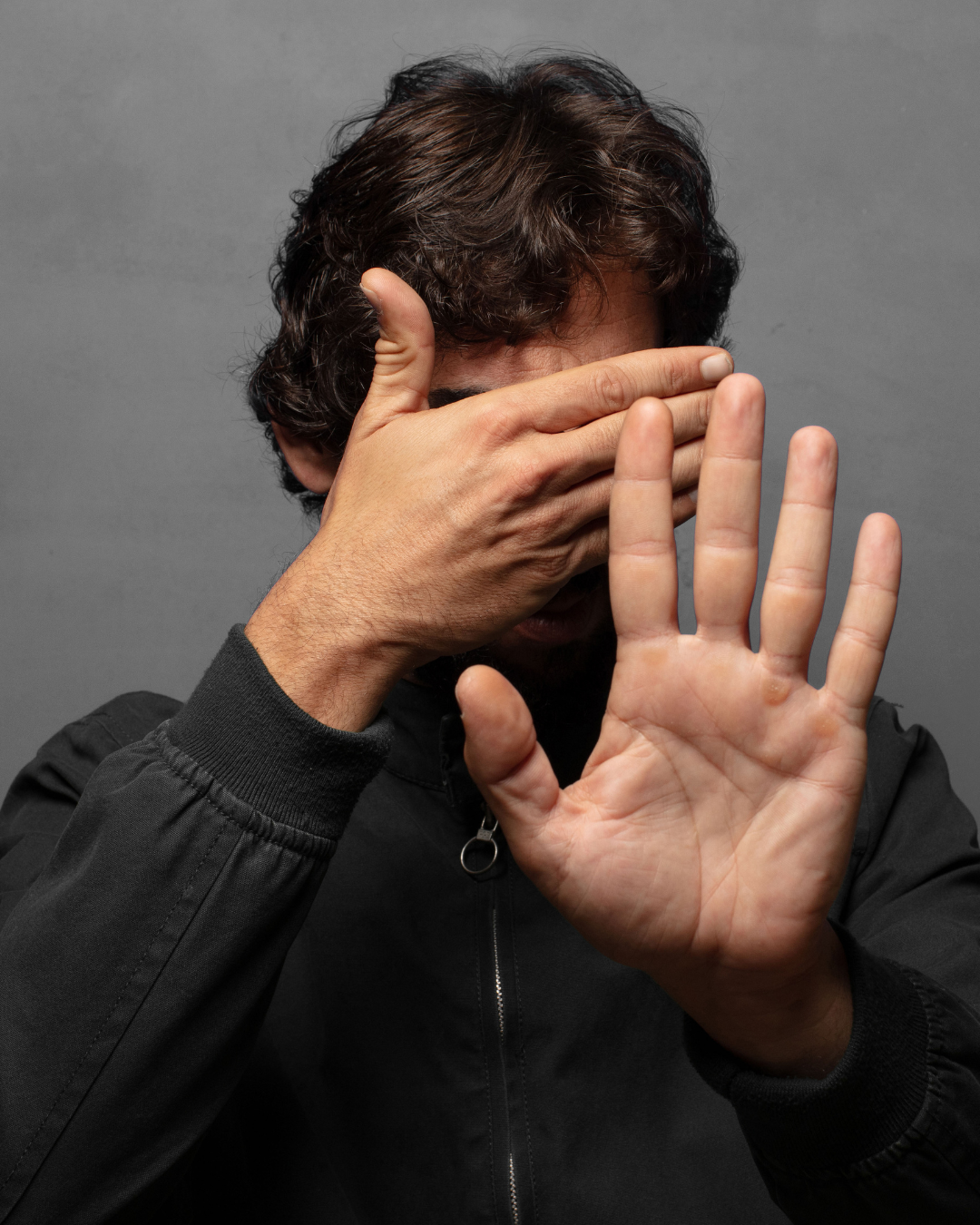 Mann in schwarzer Jacke wendet sich ab und verdeckt sein Gesicht mit der Hand – Symbolbild für Bindungsangst, Rückzug und emotionale Abwehr in Beziehungen.