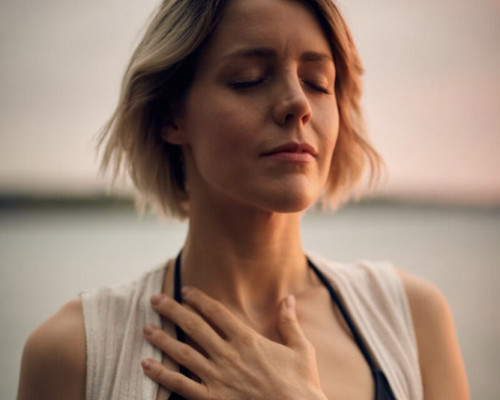 Titelbild des Kurses Das Kind in dir muss Heimat finden. Darauf ist eine Frau zu sehen, die ihre Hand auf ihr Herz legt und ihre Augen geschlossen hat.