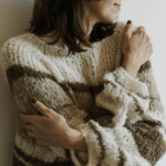 Frau, die sich selbst liebevoll im Arm hält, da sie sich selbst akzeptiert und liebt. Sie strahlt Selbstakzeptanz aus.