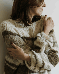 Frau, die sich selbst liebevoll im Arm hält, da sie sich selbst akzeptiert und liebt. Sie strahlt Selbstakzeptanz aus.