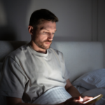 Mann, der im Bett sitzt und am Handy prokrastiniert. Er zeigt ein klares Bild von Selbstabotage.