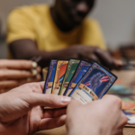 Tut Spielen der Psyche gut? Warum Erwachsene das Spielen verlernen und wiederentdecken sollten 13 Nahaufnahme einer Person, die Spielkarten in der Hand hält und gemeinsam mit anderen ein Gesellschaftsspiel am Tisch spielt.