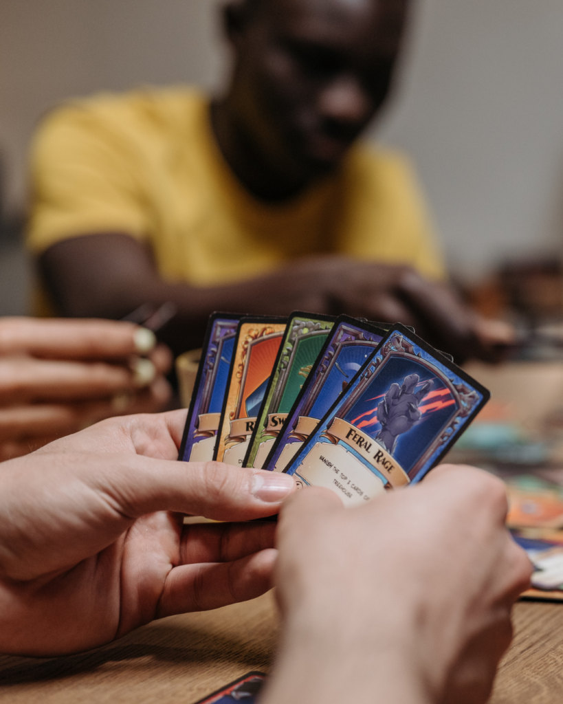 Nahaufnahme einer Person, die Spielkarten in der Hand hält und gemeinsam mit anderen ein Gesellschaftsspiel am Tisch spielt.