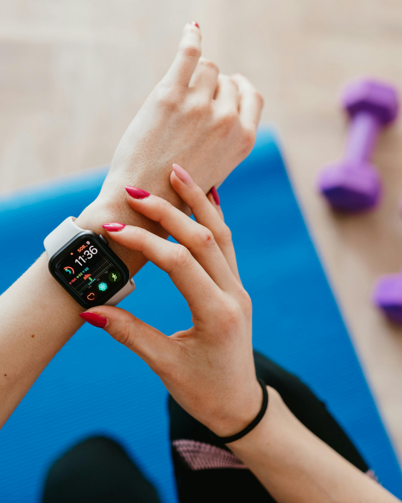 Nahaufnahme einer Frau, die vor dem Sport ihre Smartwatch auf einer blauen Fitnessmatte überprüft. Der Fitness-Tracker zeigt Aktivitätsdaten und Trainingsziele an und steht symbolisch für digitales Gesundheitstracking, Selbstoptimierung und die Kontrolle der eigenen Bewegung.